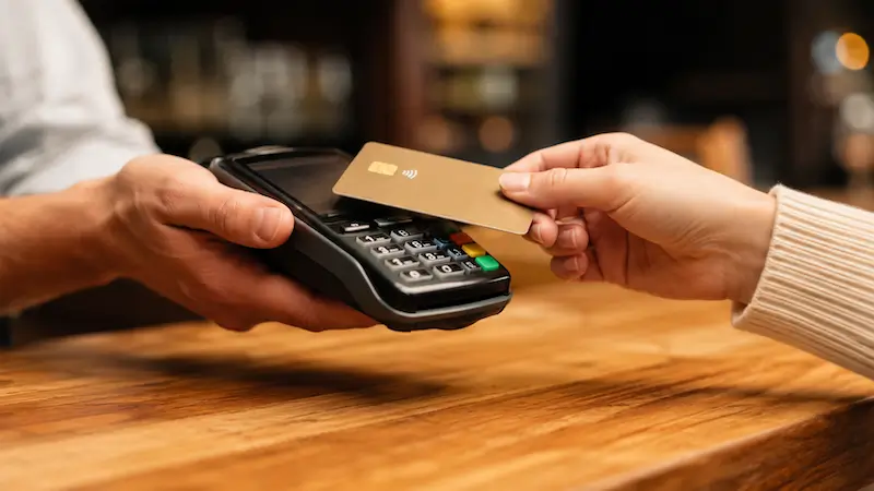 Une cliente approche sa carte bancaire du terminal de paiement que lui tend le commerçant, au comptoir